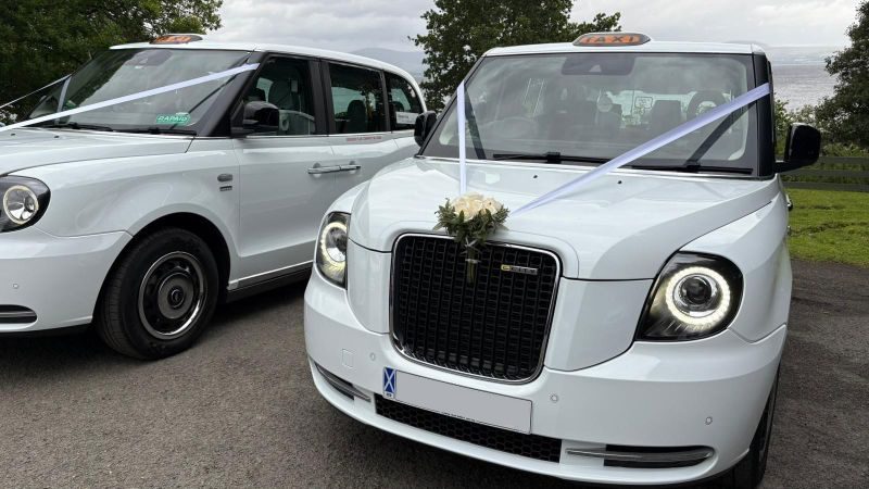 Two white electric wedding cabs with ribbons and flowers